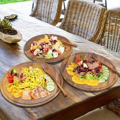 three wooden plates filled with food sitting on top of a table next to a bowl of fruit