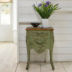 a small green cabinet with flowers on top and a vase sitting on it's side