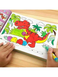 a child's hands holding a pencil and drawing a dinosaur book