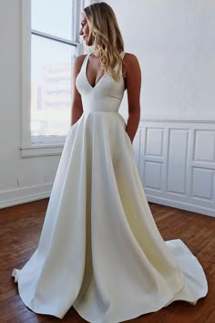 a woman standing in front of a window wearing a white wedding dress with deep v - neck