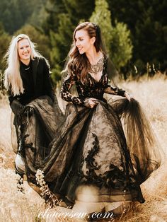 two women in long black dresses walking through tall grass