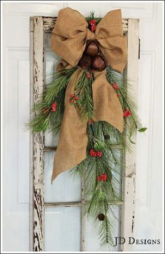 an old window decorated with evergreen, pine cones and burlocks is hung on the front door