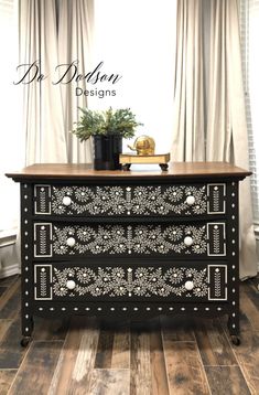 a black and white dresser sitting on top of a wooden floor next to a window