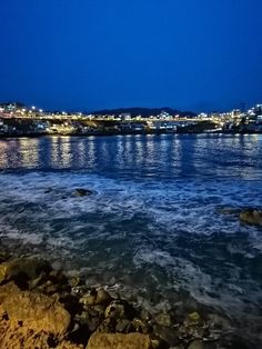 the city lights are lit up in the distance from the water's edge at night