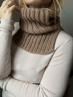 a blonde woman wearing a knitted cowl neck sweater and holding her hand on her hip