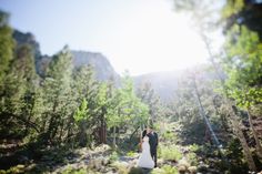 a bride and groom walking through the woods