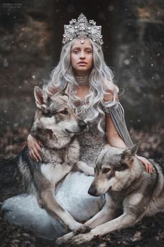 a woman sitting on the ground next to two wolfs wearing tiara and dress