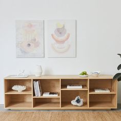 two paintings hang on the wall next to a wooden shelf with books and vases