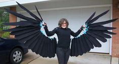 a woman standing in front of a garage holding two large black wings over her shoulders