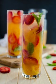 two glasses filled with drinks sitting on top of a wooden table next to strawberries