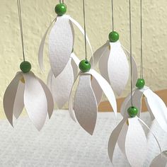 four white paper flowers hanging from strings with green bead caps and leaves on them