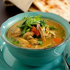 a blue bowl filled with soup on top of a green saucer next to bread