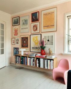 a living room filled with lots of books and pictures on the wall next to a pink chair