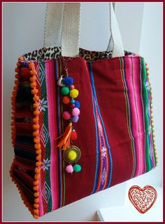 a colorful handbag hanging from the side of a wall with pom poms on it