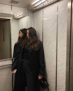 two women standing next to each other in front of a mirror on a bathroom wall