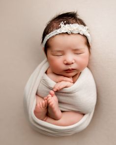 a newborn baby is wrapped in a blanket and wearing a headband with flowers on it