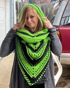 a woman wearing a green and black crocheted shawl in front of a red car