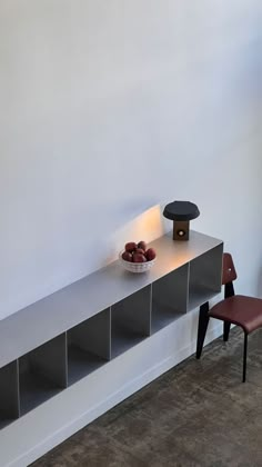 a bowl of fruit sitting on top of a white shelf next to a red chair