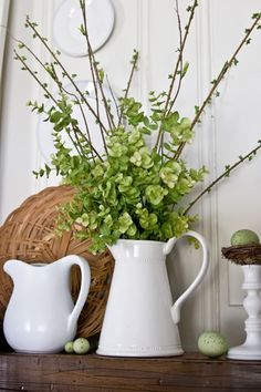 a white pitcher and vase with green flowers on a mantel