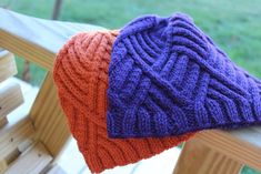 two knitted hats sitting on top of a wooden bench