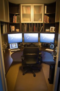 a computer desk with two monitors and a laptop on it in front of bookshelves