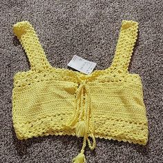 a crocheted yellow top is laying on the floor with a tag attached to it