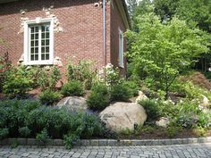 a brick house with landscaping around it and trees in the front yard, along with flowers and rocks