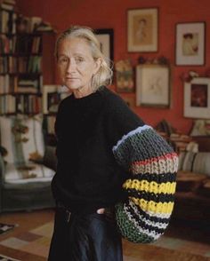 an older woman is standing in her living room holding a large knitted sweater over her shoulder