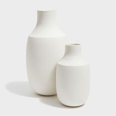 two white vases sitting next to each other on a white surface with no one around them