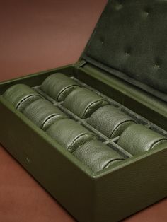 an open green leather box with six rolls in it on a table top next to a brown surface