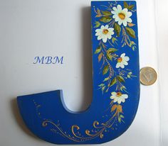 the letter j is painted with flowers and leaves on blue paint, next to a quarter penny