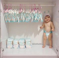 a baby in a diaper standing next to a shelf filled with diapers