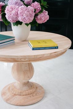 a wooden table with books on it and pink hydrangeas in the vase next to it