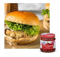 a chicken sandwich with cheese and lettuce next to a jar of chili sauce