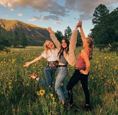 three young women are dancing in a field full of wildflowers