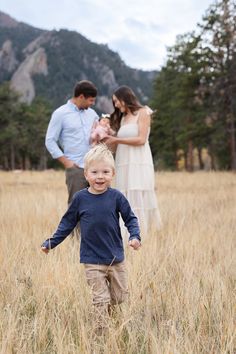 a little boy running through tall grass with his parents