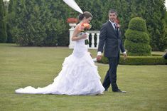 a bride and groom are walking through the grass in front of an arch decorated with flowers