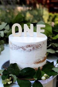 a white cake sitting on top of a table covered in greenery and wooden letters