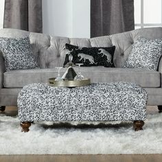 a living room with a couch, ottoman and coffee table in front of a window