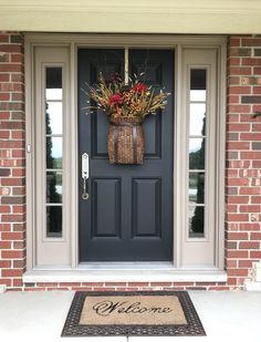 a welcome mat is placed in front of a blue door with a basket full of flowers