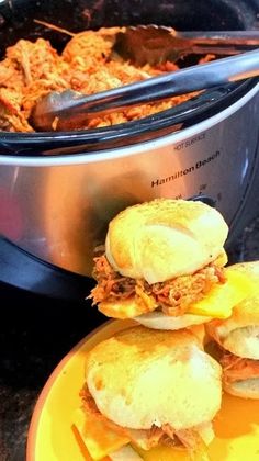 two sandwiches are sitting on a plate next to a crock pot filled with sauce