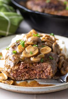 a piece of meatloaf covered in mushrooms on top of mashed potatoes and gravy