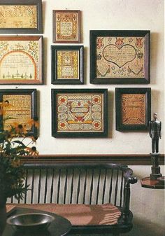 there are many framed pictures on the wall next to a bench and vase with flowers