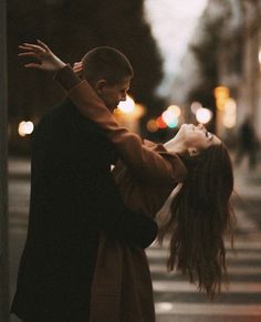 a man and woman are dancing on the street at night with their arms around each other