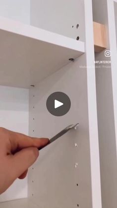 someone is holding a pair of scissors in the corner of a book shelf with holes on it