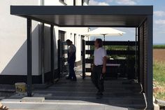 two men are standing under an open umbrella in front of a white building with black shutters