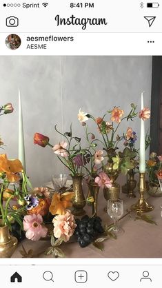 a table topped with lots of vases filled with flowers next to candles and candlesticks