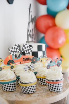 cupcakes with white frosting and race cars on them sitting on a table