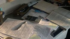 many papers are spread out on a desk with a calculator, pen and cup