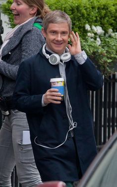 a man with headphones is talking on his cell phone while holding a coffee cup